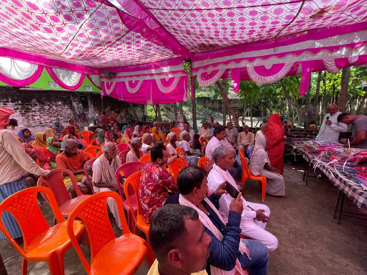 2024 के मौसमी वस्त्र वितरण में गुलाबी शामियाने के नीचे बैठे ग्रामीण।