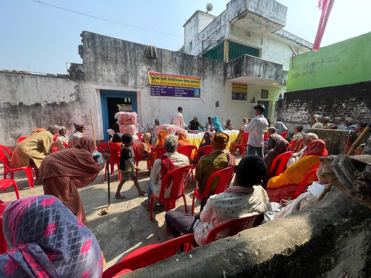 2025 के शीतकालीन कंबल वितरण में संस्था के बैनर के नीचे आँगन में मौजूद ग्रामीण।